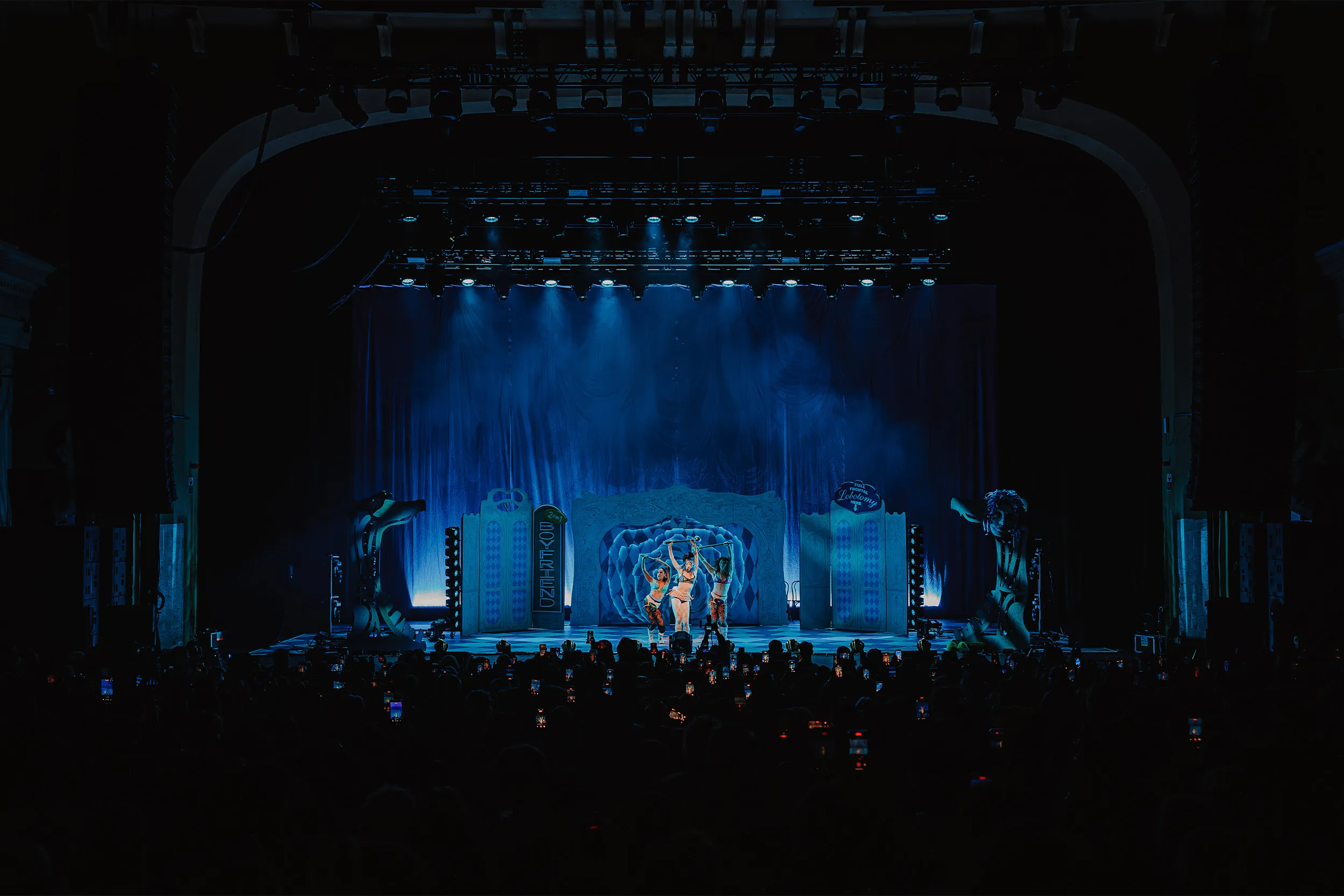 The venue from the back of the room: the lighting rig overhead, the set in blue haze and a packed floor