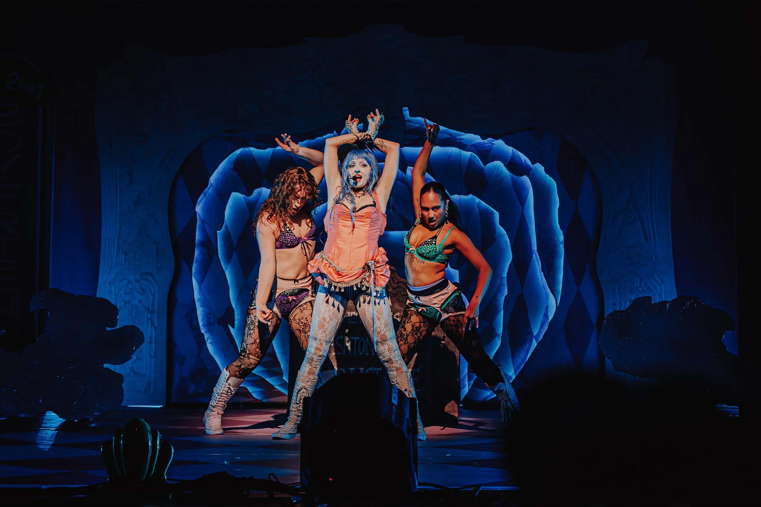 Ashnikko and two dancers posed with arms raised in front of a blue harlequin rose