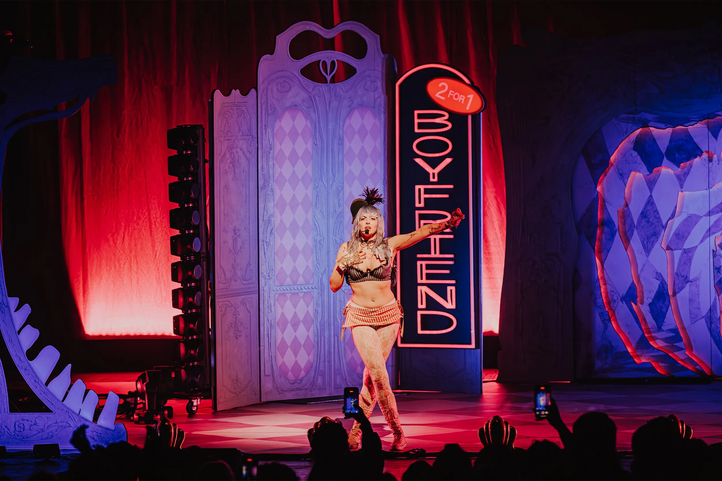 Ashnikko pointing out to the crowd beside the neon Boyfriend 2 for 1 sign, red drapes behind