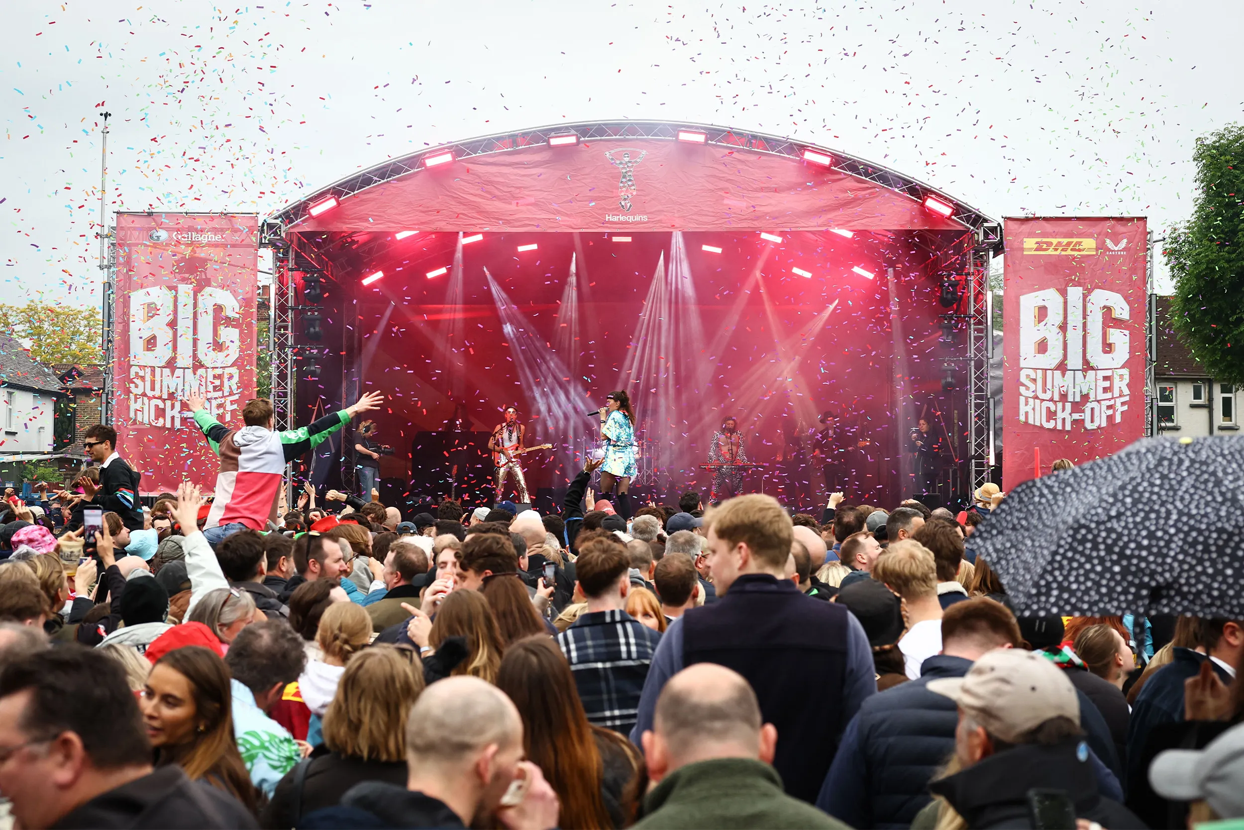 Confetti over a packed fan zone in front of a red-lit outdoor stage flanked by Big Summer Kick-Off banners
