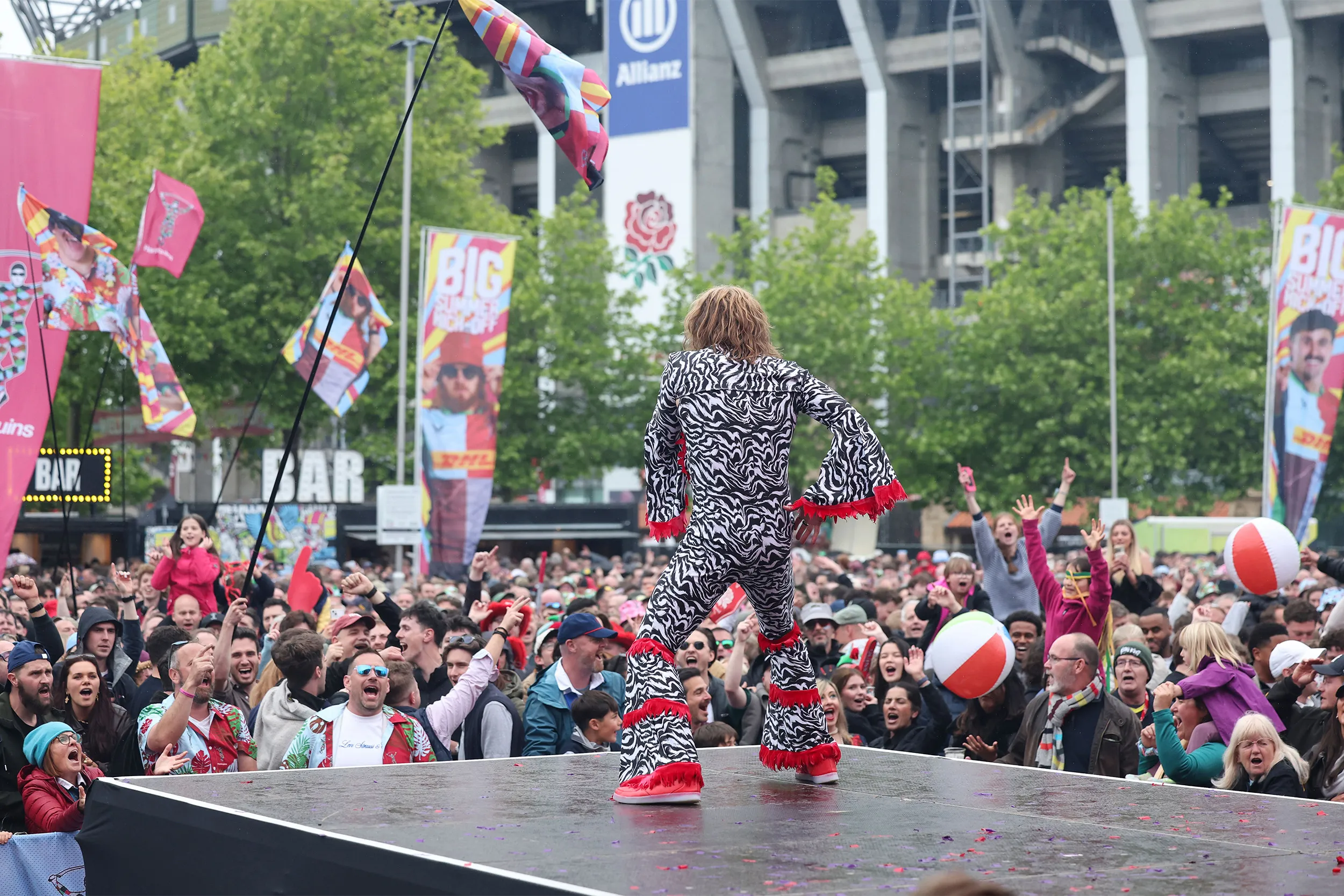 The zebra-print performer from behind on a small stage, the fan zone crowd and banners in front
