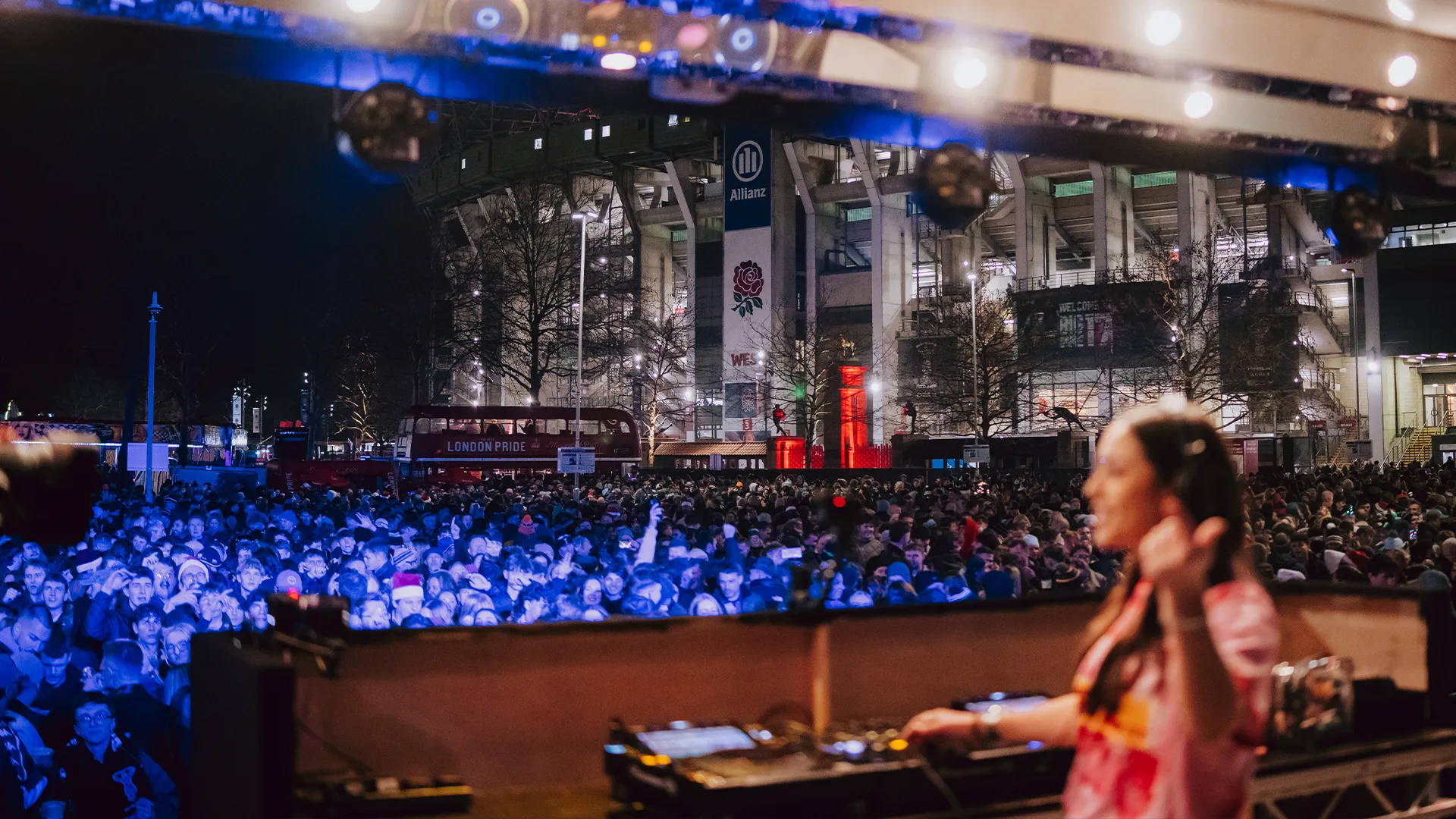 A DJ set overlooking a packed fan zone outside the stadium at night