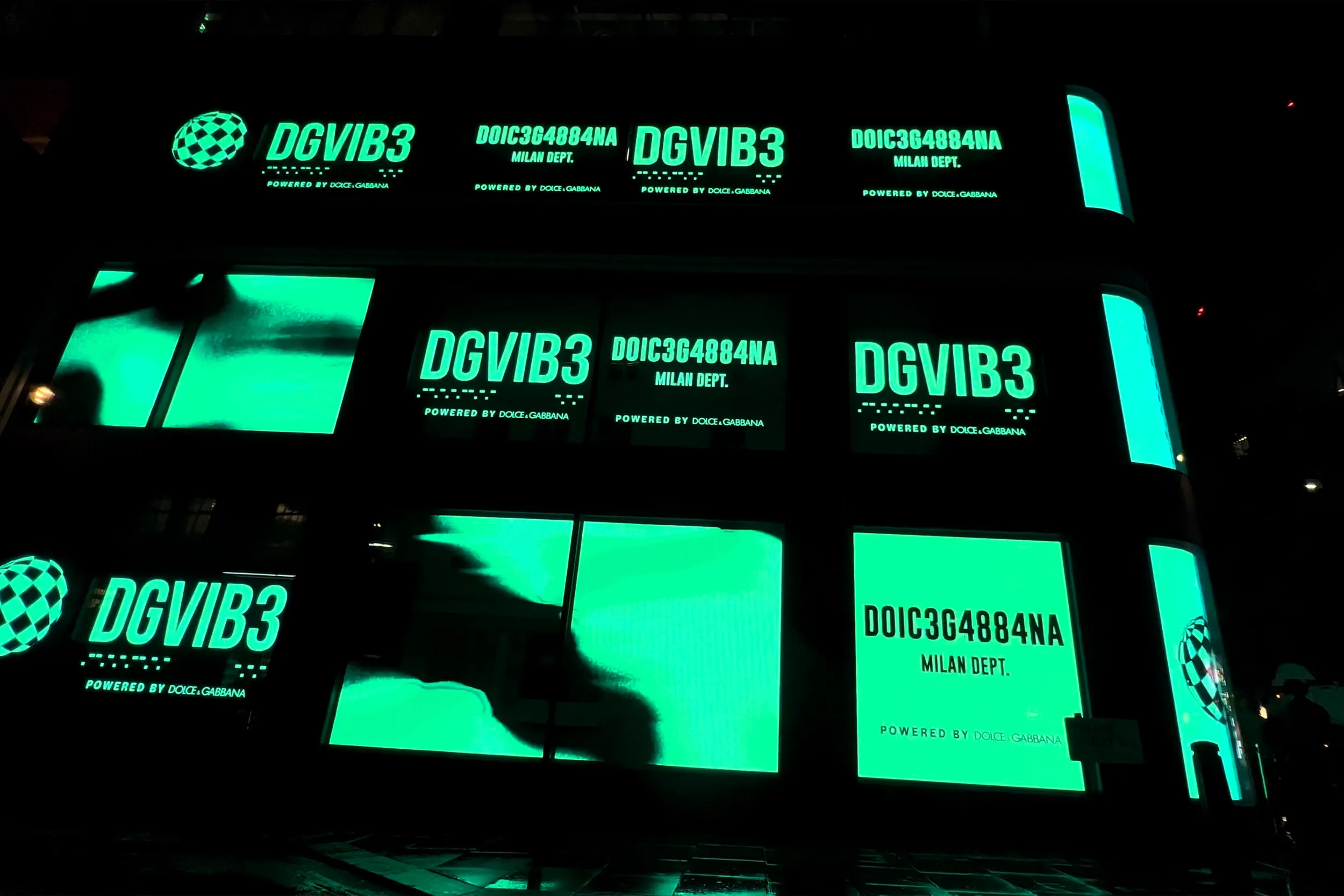 A building facade covered in green screens showing DGVIB3 branding at night