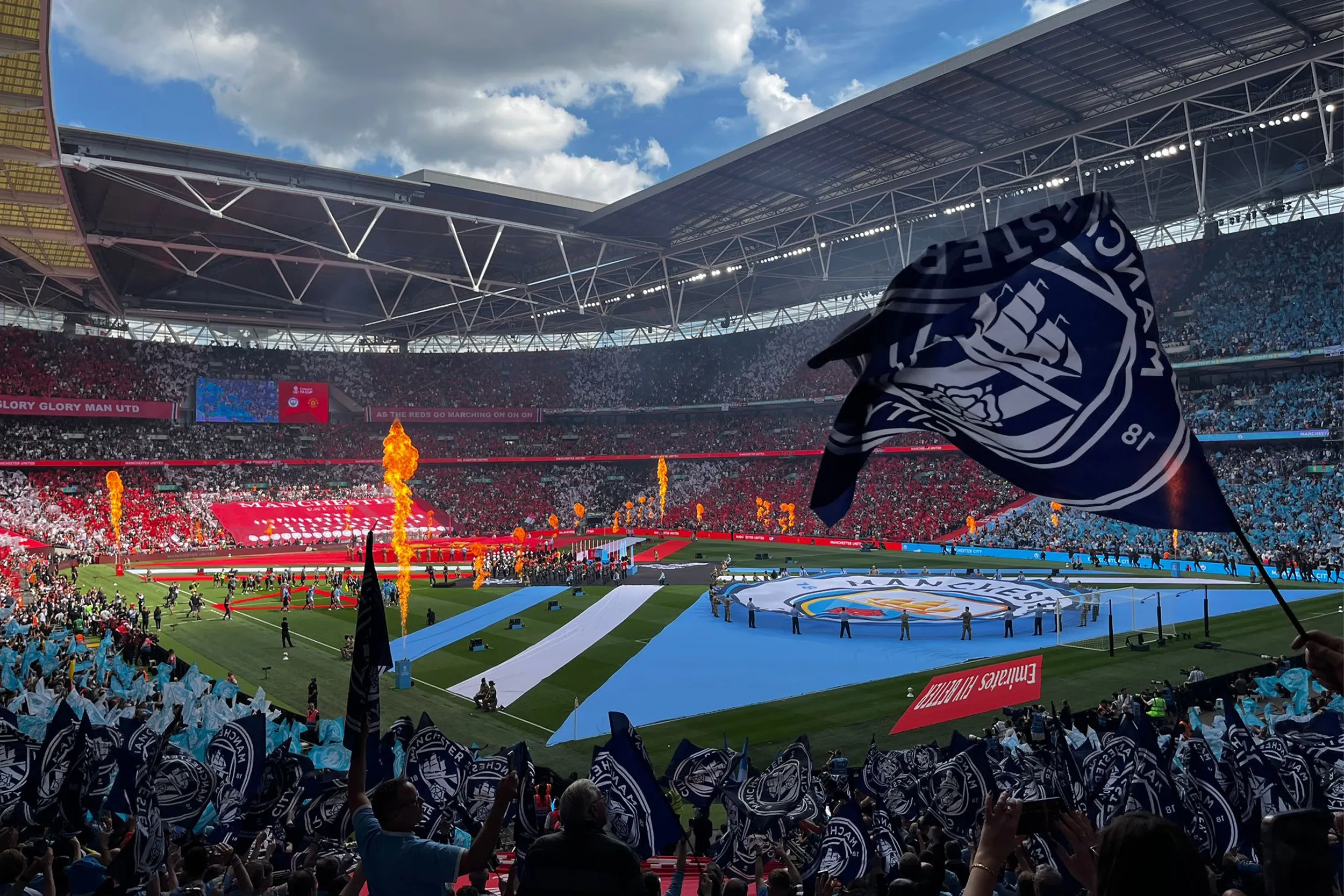 Supporters waving flags in the stands as flames rise from the pitch-side display at Wembley