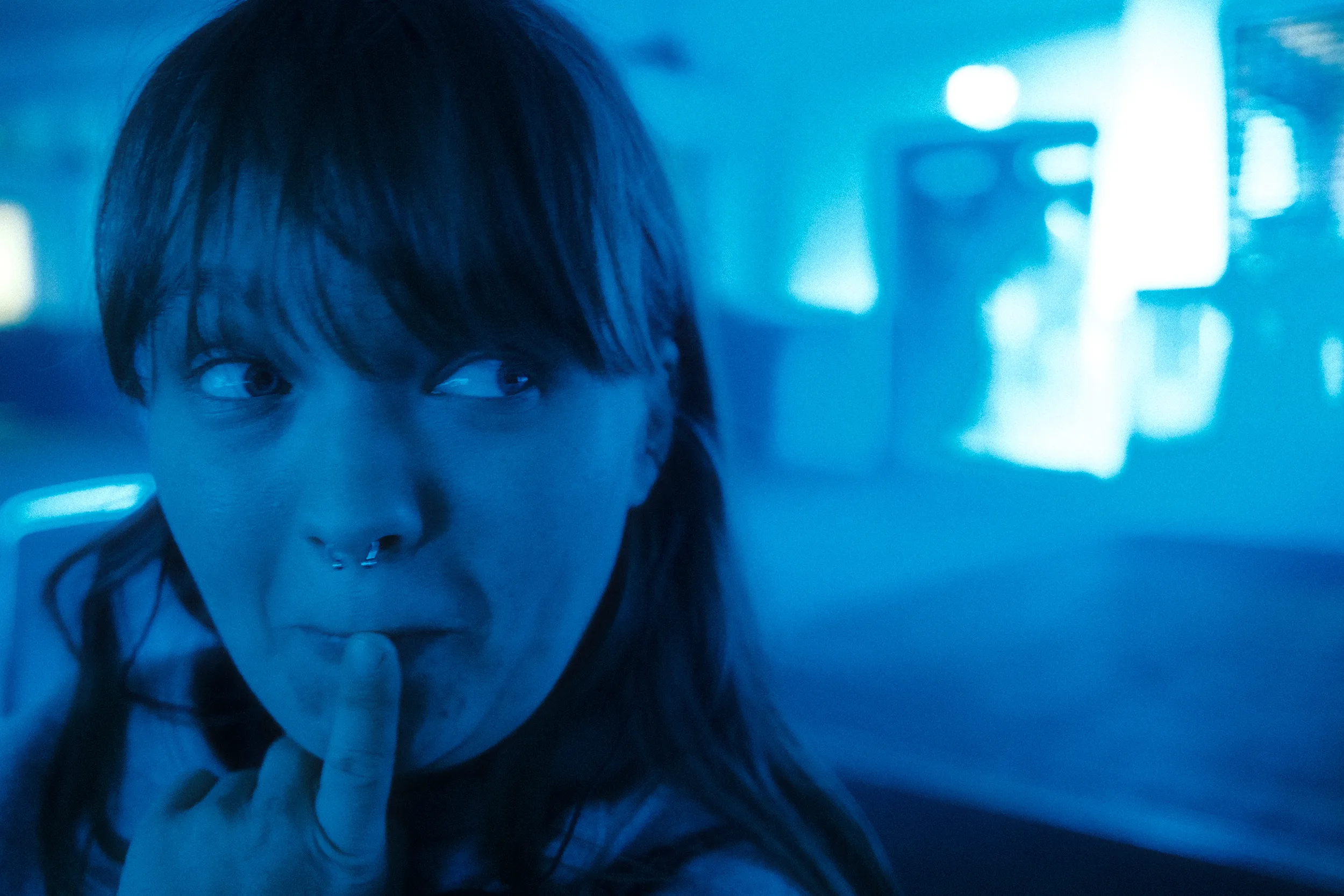 Holly lit in blue, finger to her lips with a playful look