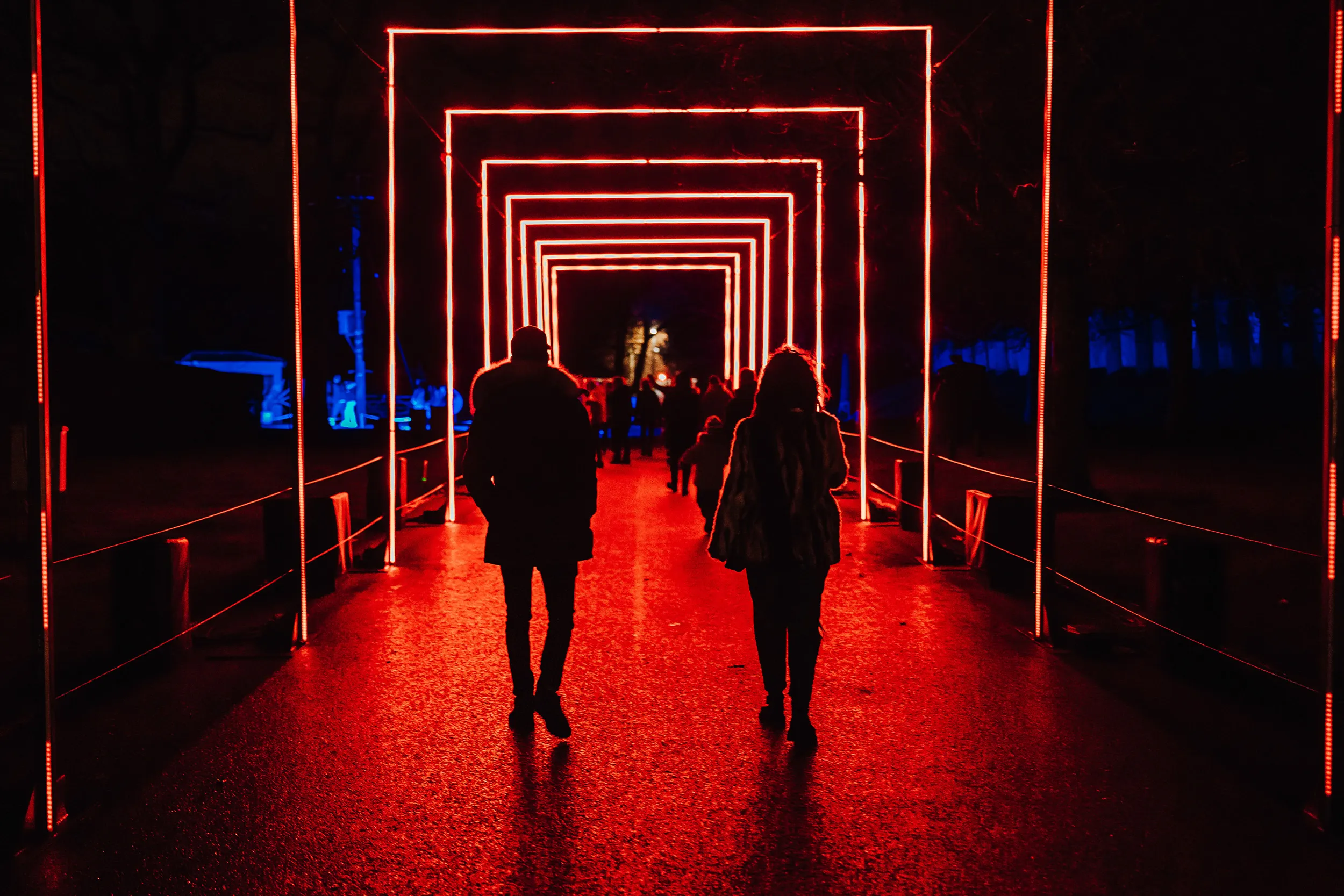 Two visitors walking down a path through a tunnel of red neon frames