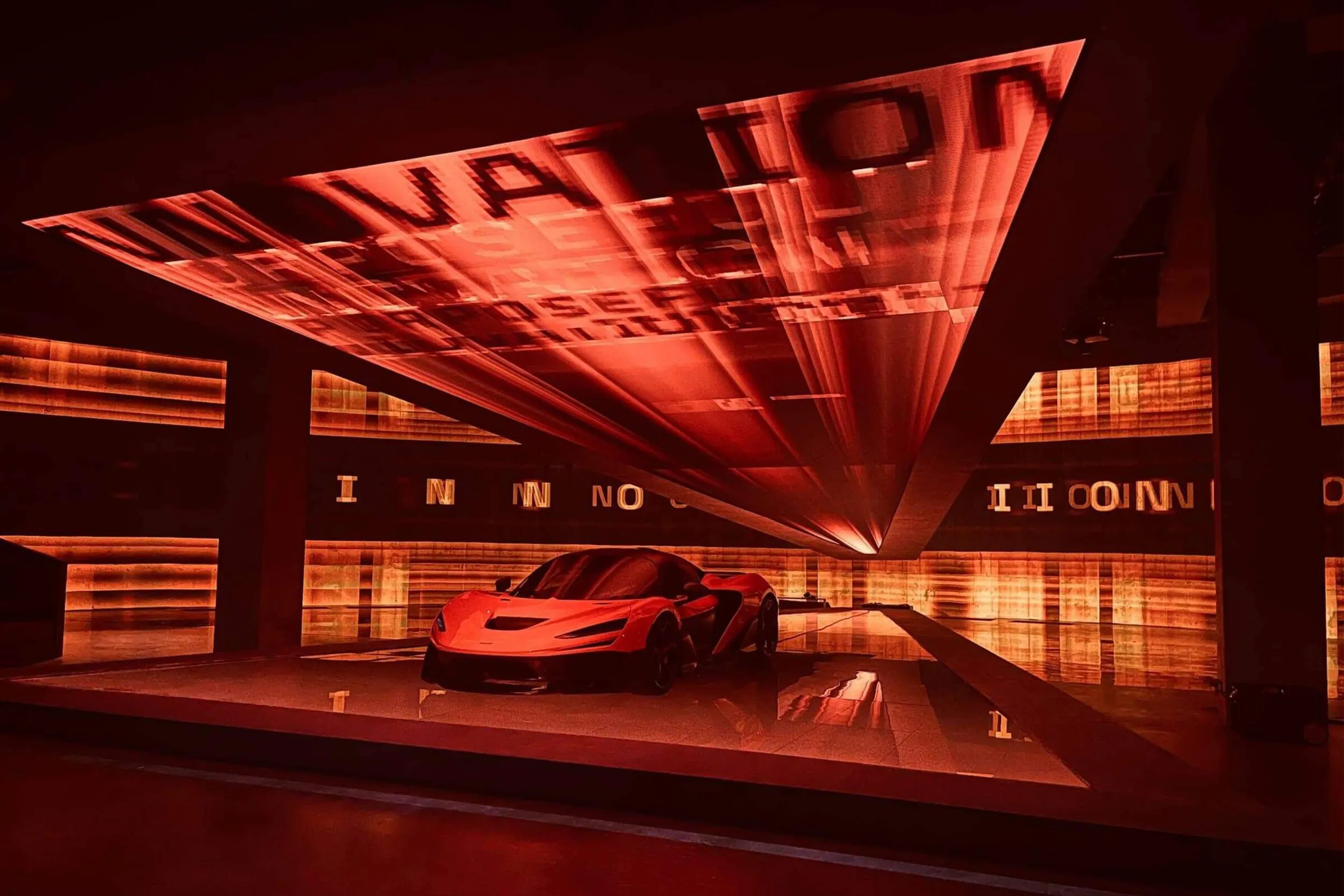 The car beneath a vast angled canopy of red projected visuals