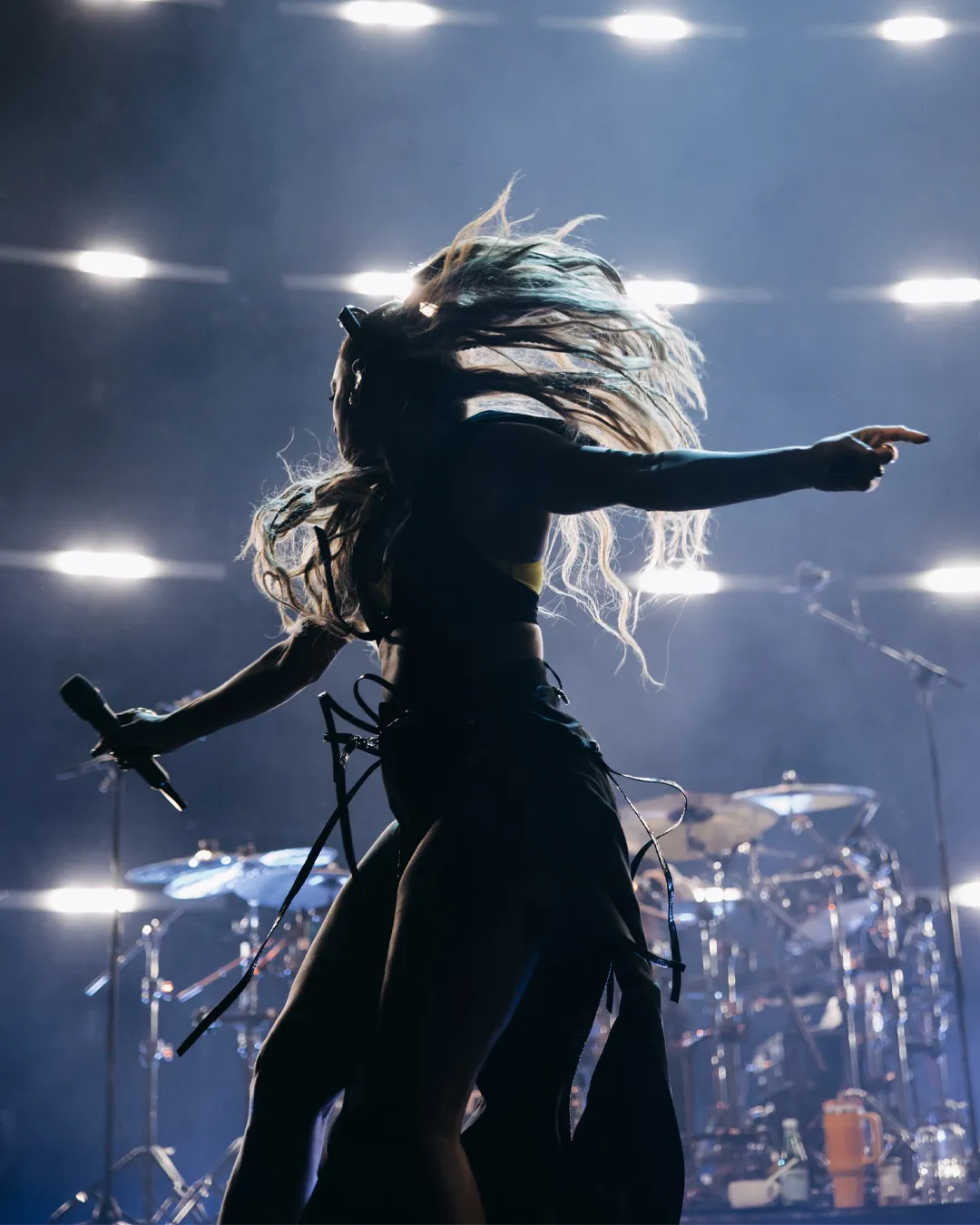 A Mis-Teeq singer mid hair flip in silhouette, one arm pointing out, against a wall of stage lights