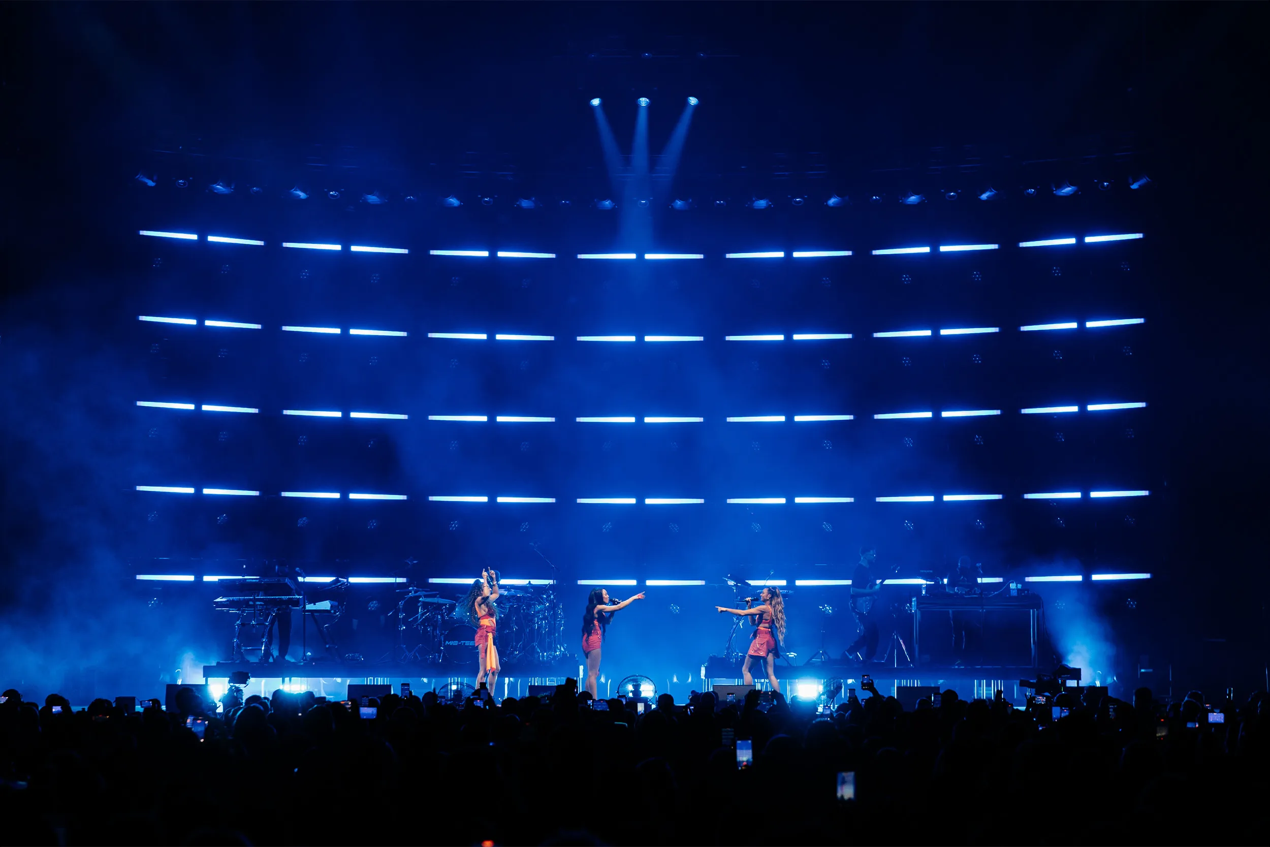 The stage in blue, the group small at the front beneath tiers of blue linear light