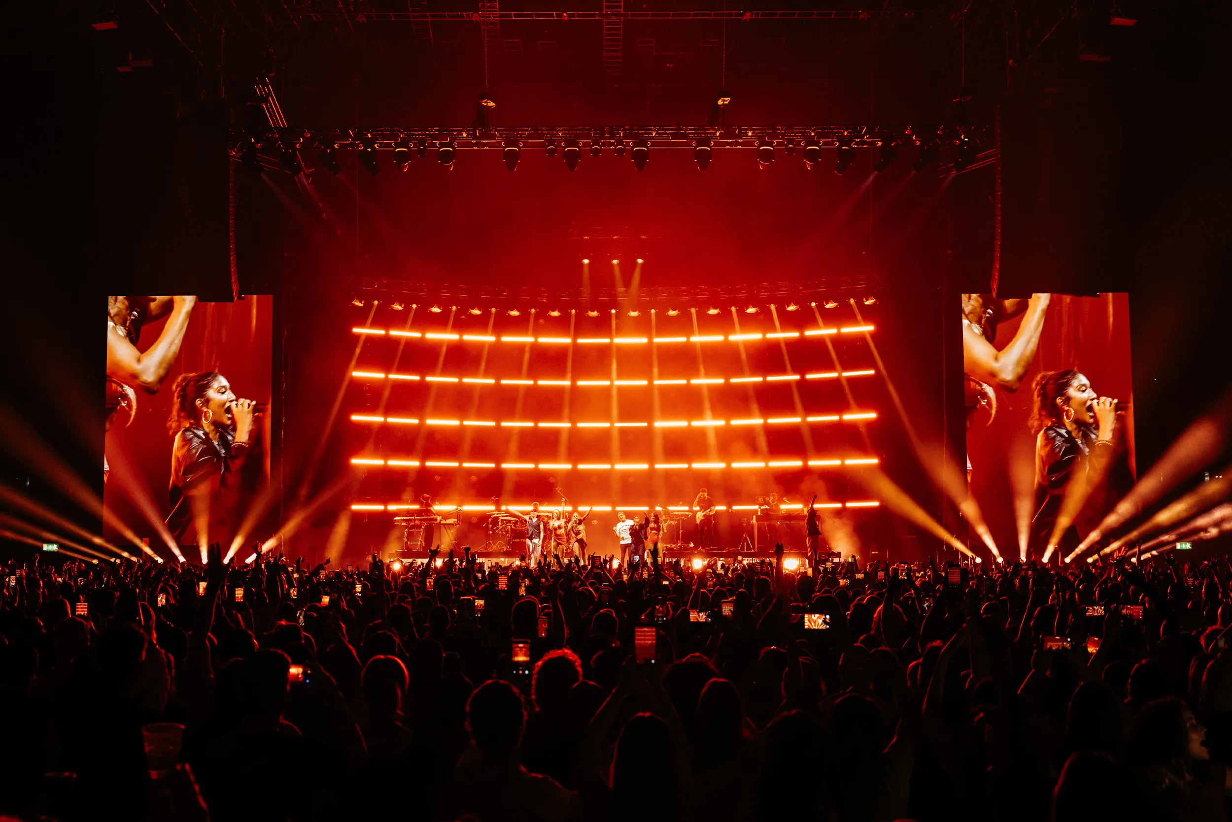 The whole stage in red, a grid of orange light rows behind the band and beams fanning out over the crowd