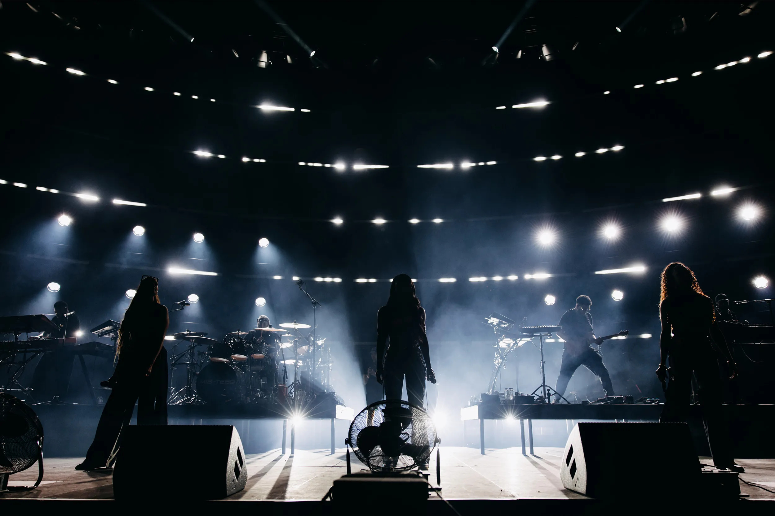 The group and band silhouetted against curved rows of white linear light and haze