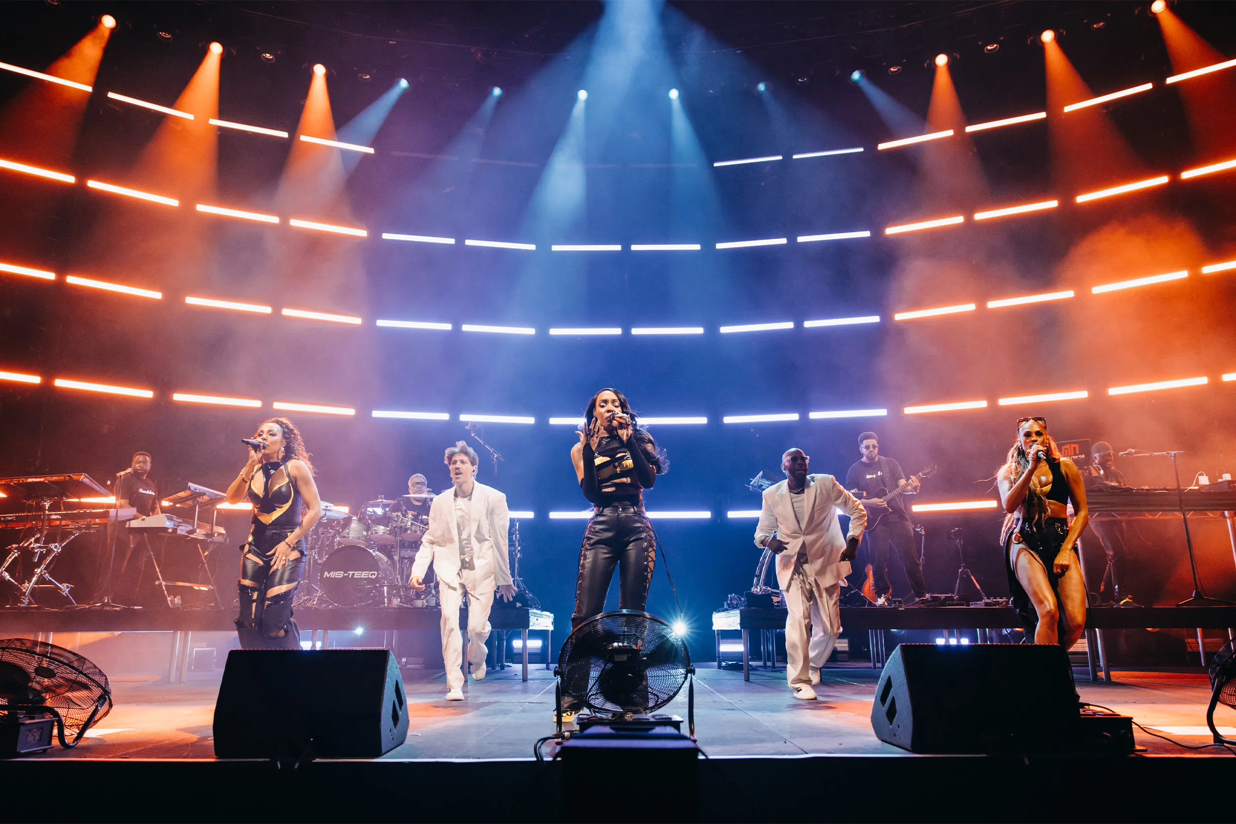 The full line-up with dancers in white suits, the curved light rows glowing orange and blue