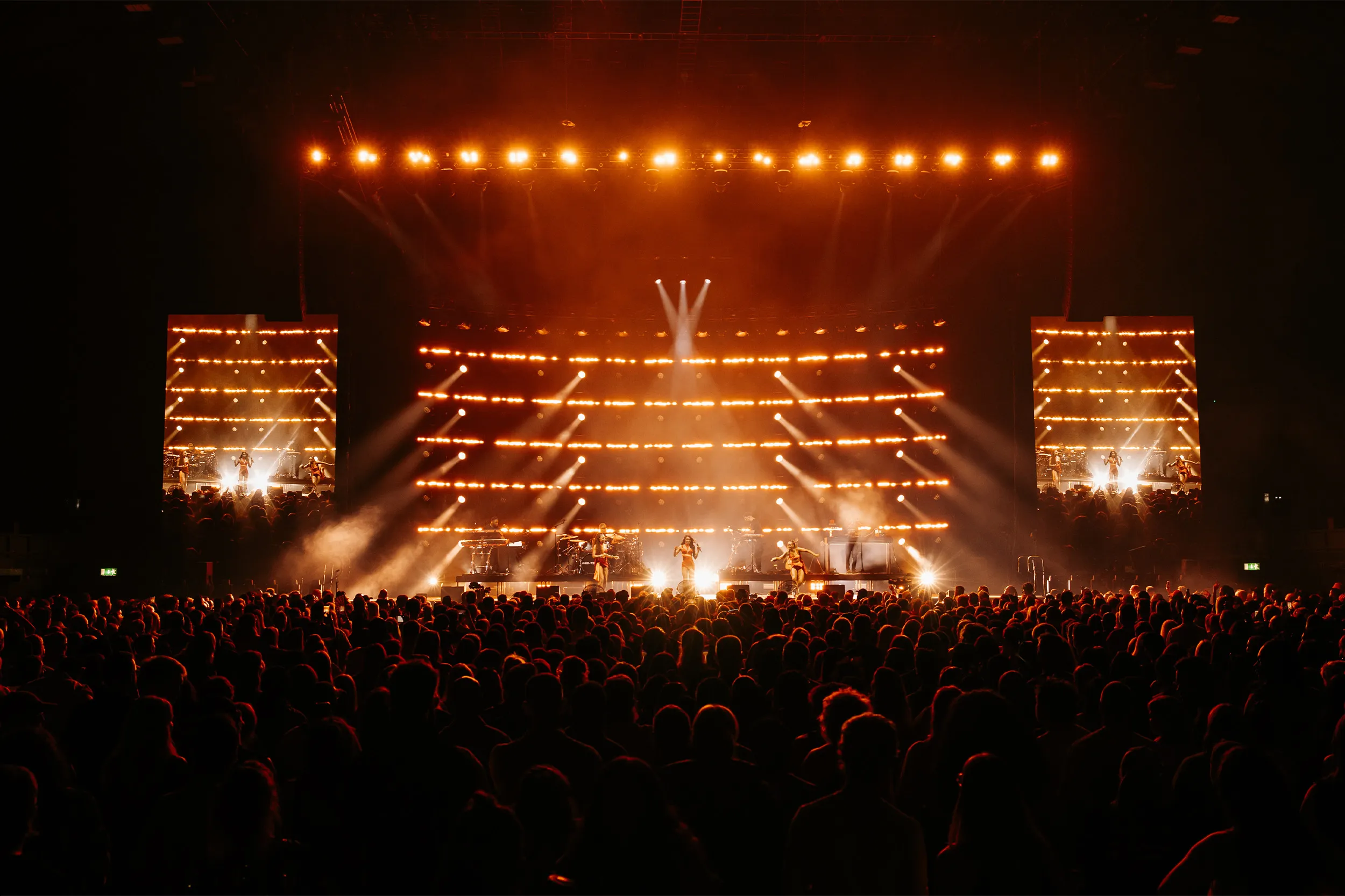 The arena from the back: the stage lit amber, a straight row of lights overhead and a full floor