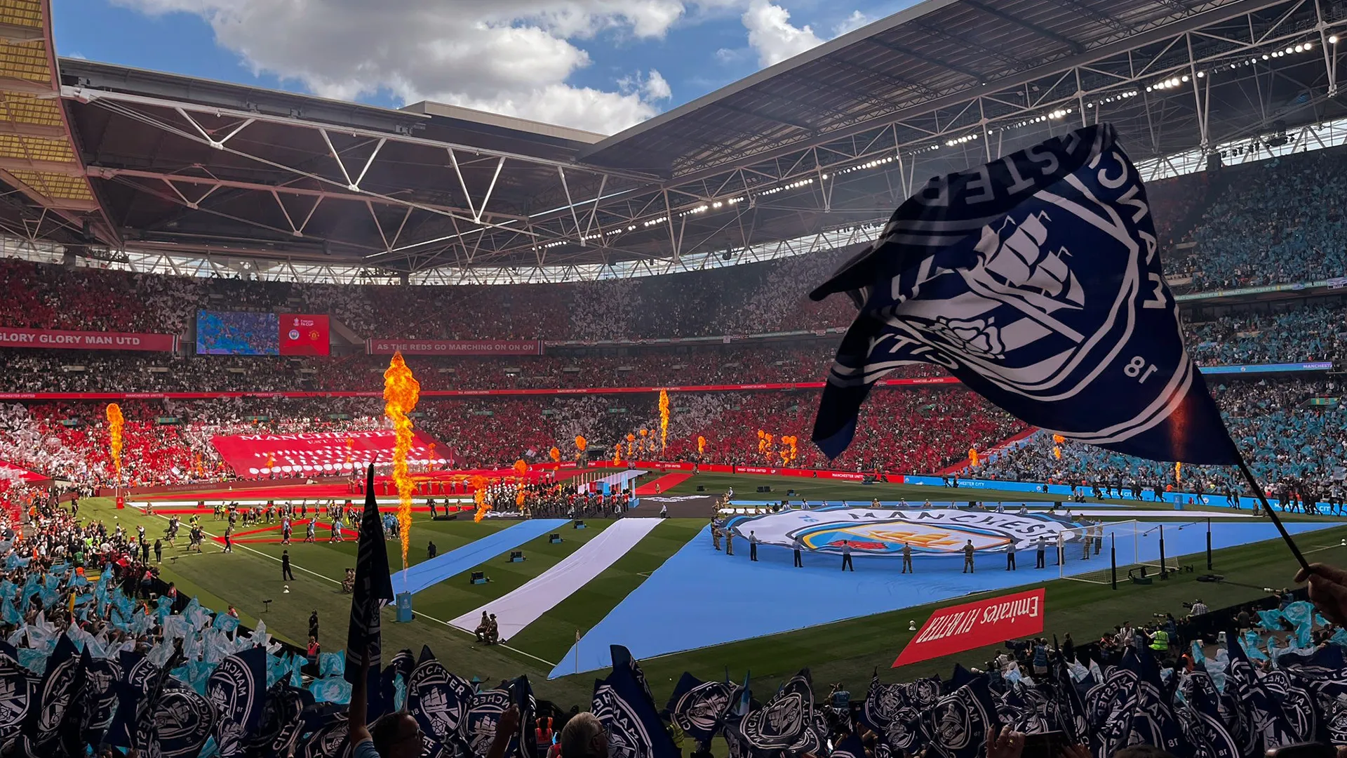 A supporters' flag waved above the crowd, pyro on the pitch behind