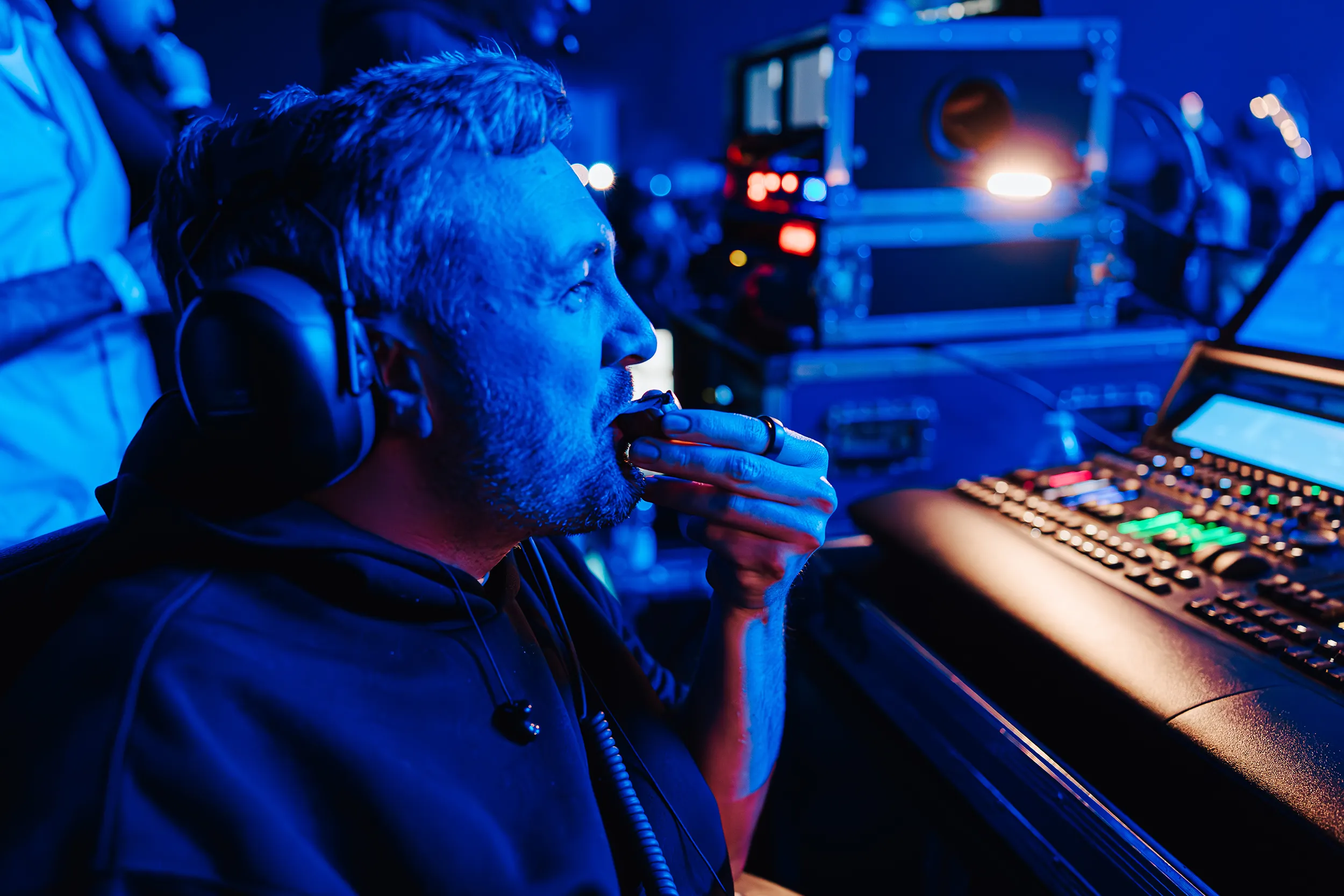Steve at the lighting desk under blue light, headphones on, eating a creme egg