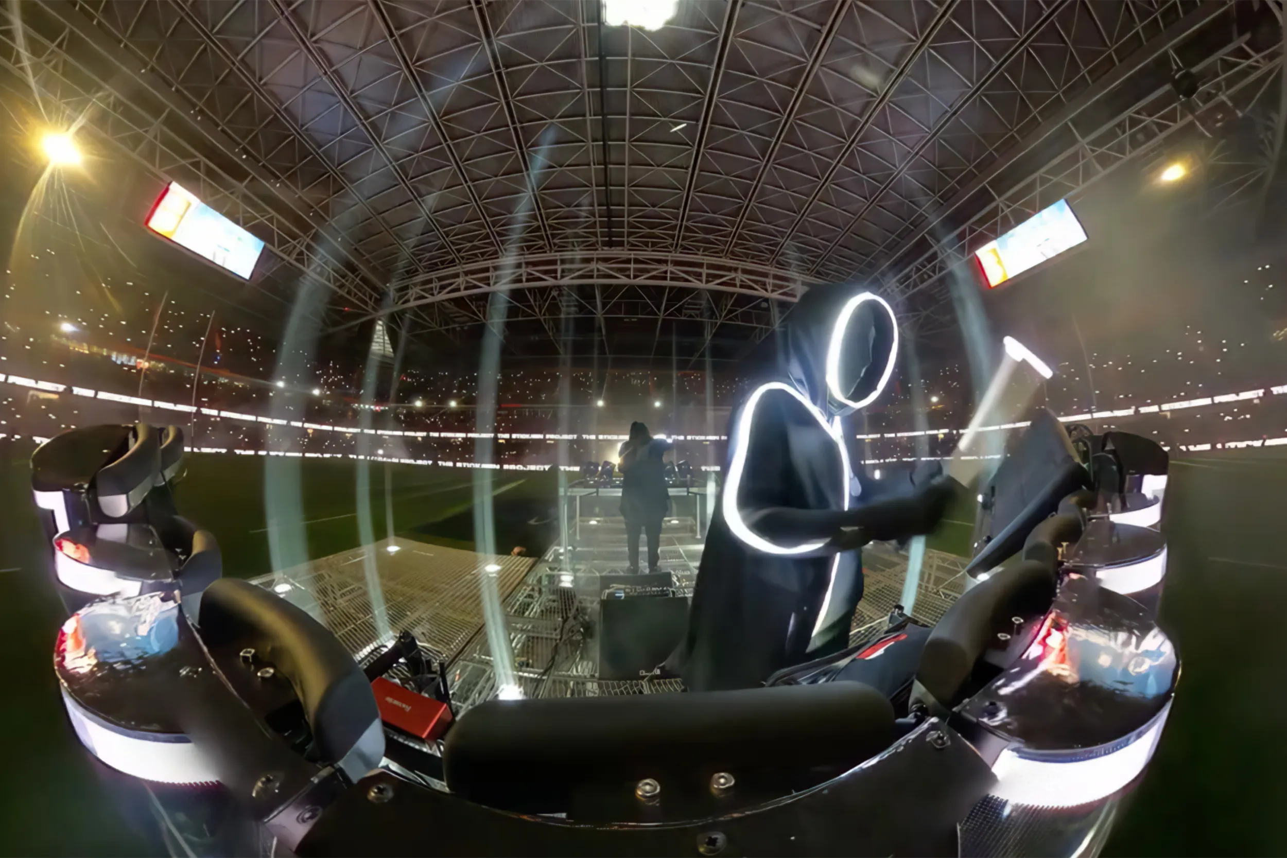 Wide-angle view from the stage: a stickman at the controls, the floodlit stadium curving around