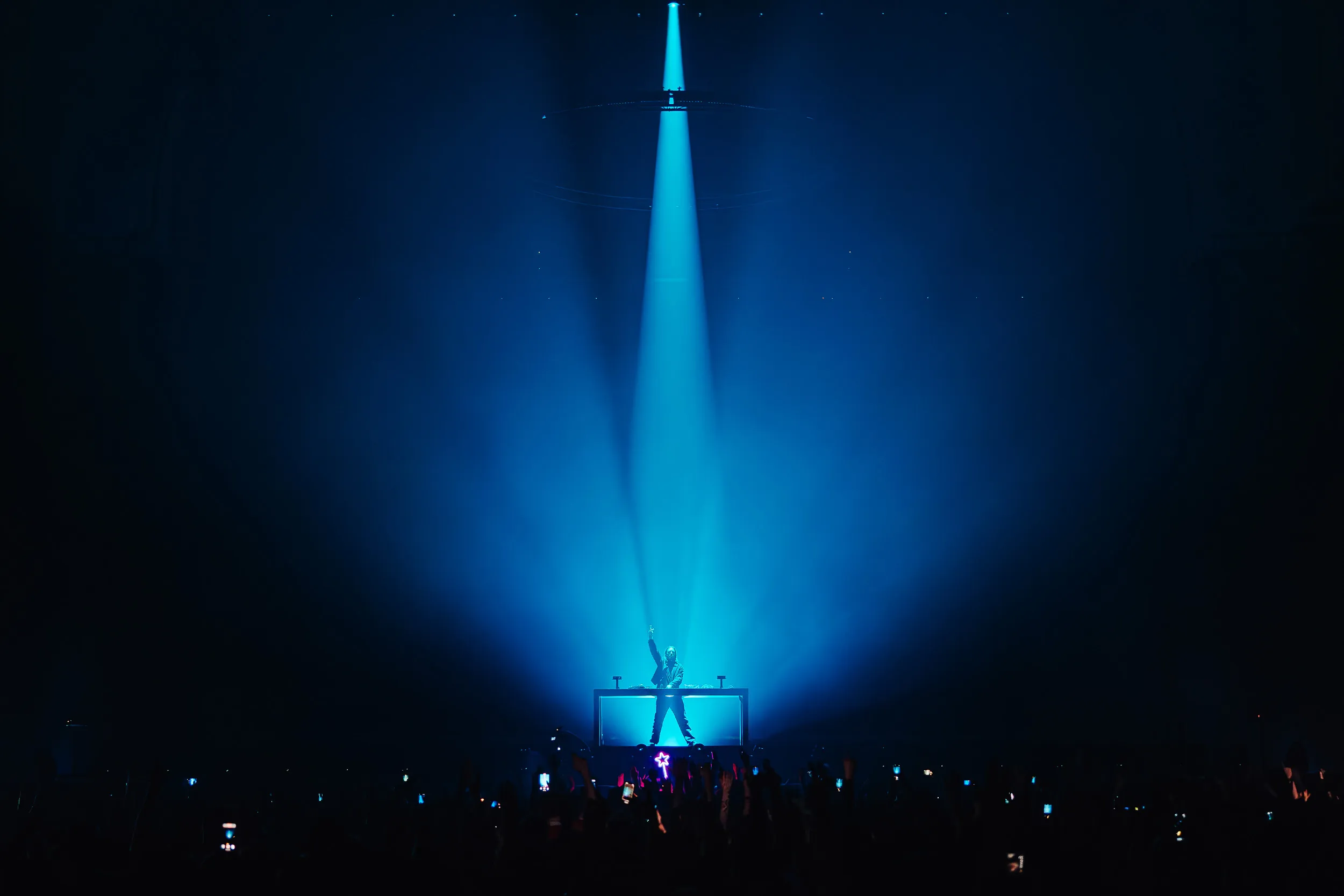Sub Focus with an arm raised at the decks, caught in one cyan shaft of light from above