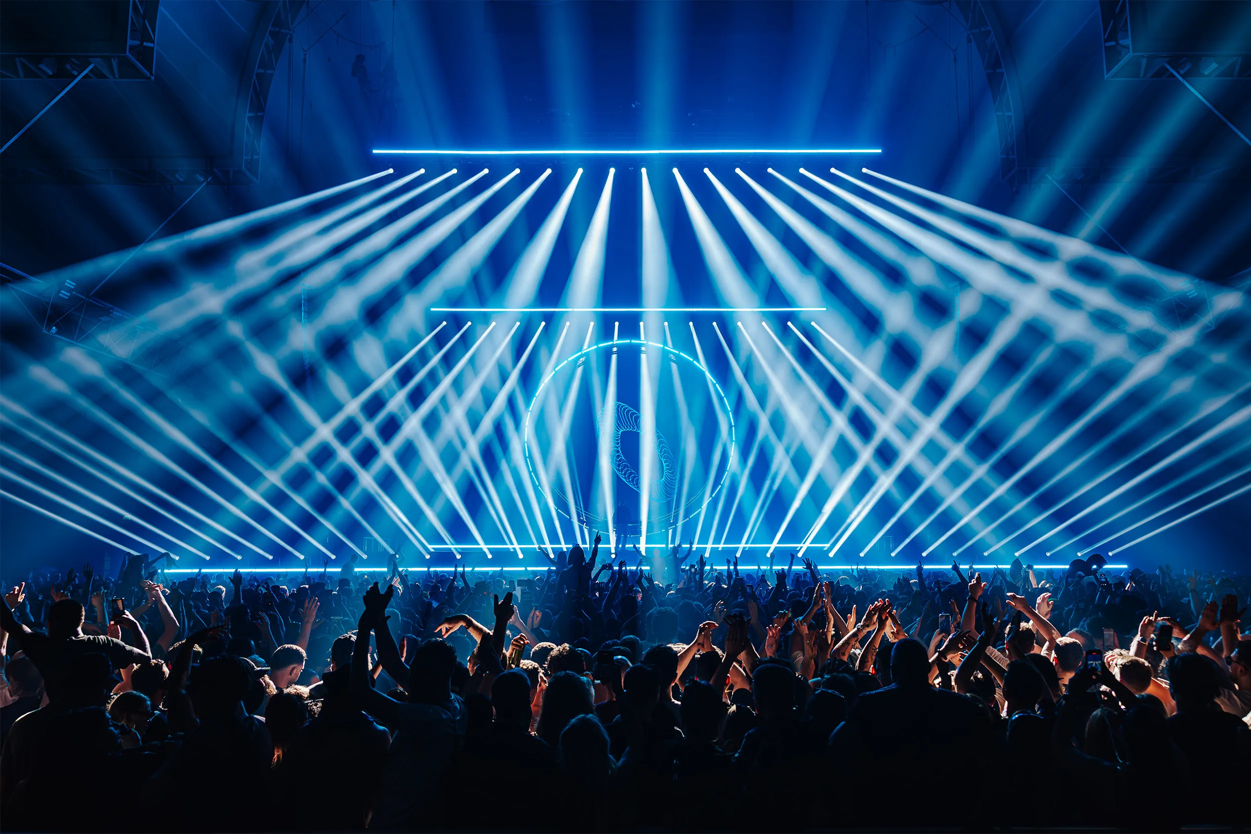 Rows of blue beams fanning over the crowd from a long linear rig