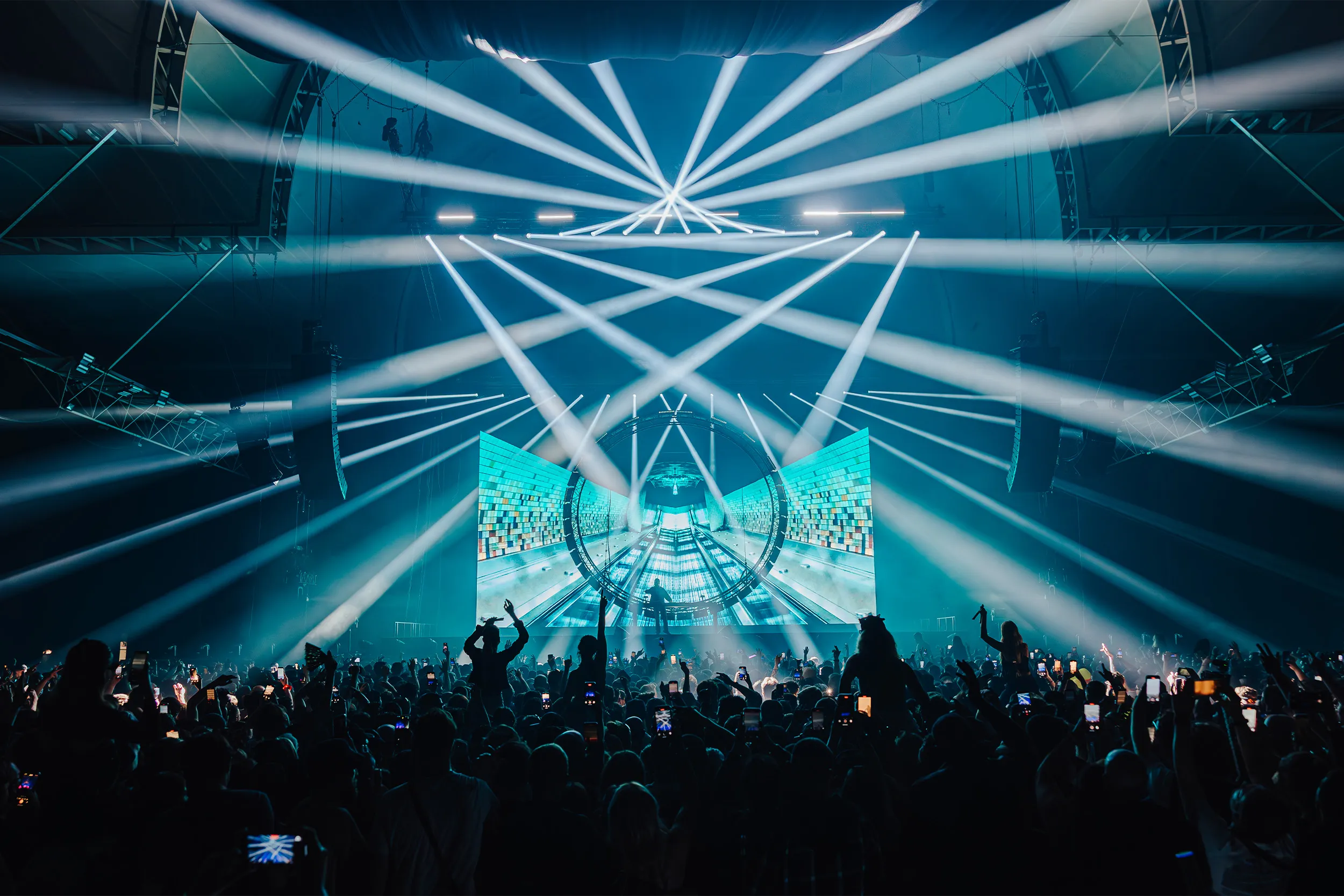 Cyan beams crossing above a curved screen, the booth at its centre