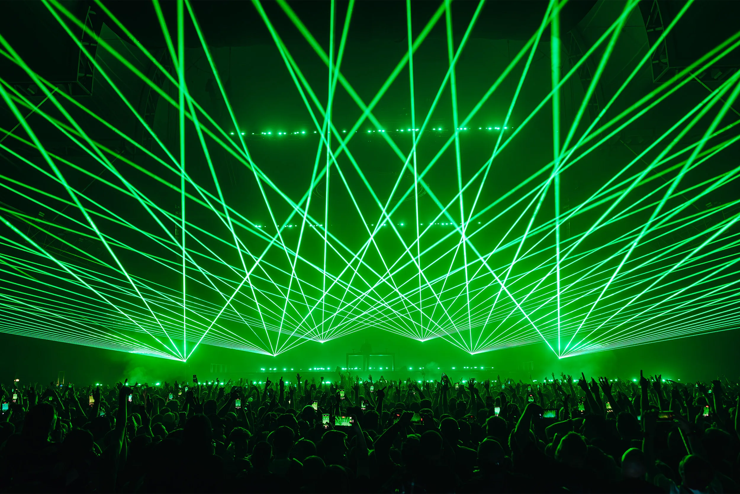 Green lasers criss-crossing the whole room above a crowd with hands in the air