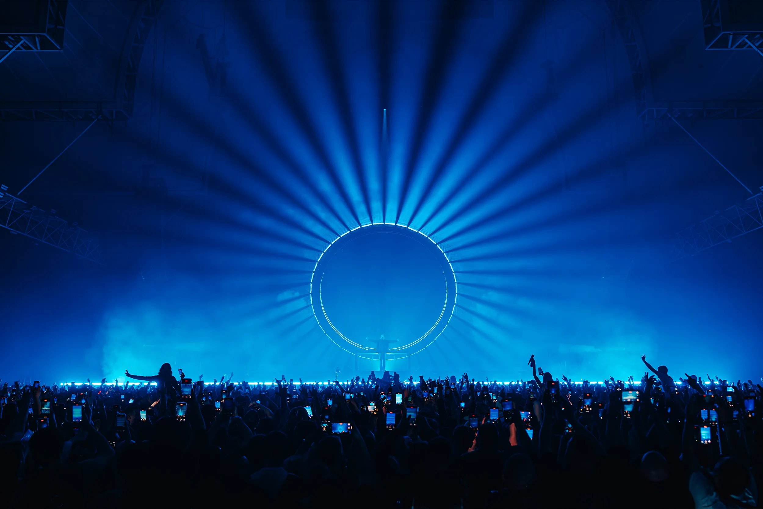 A glowing ring behind the booth with blue beams radiating out like a sunburst over the crowd