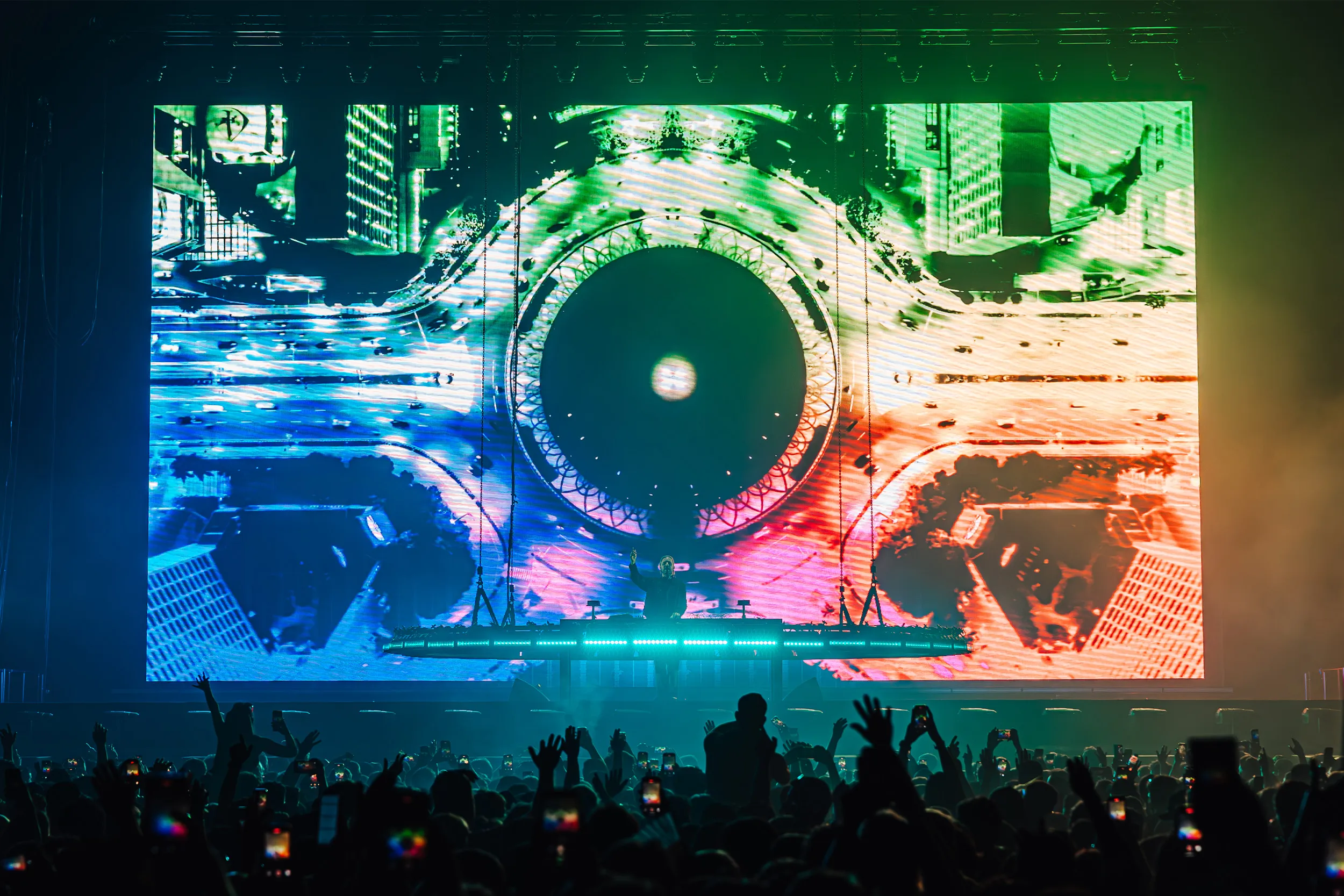 A huge screen of colourful circular visuals behind the booth, hands raised in the foreground