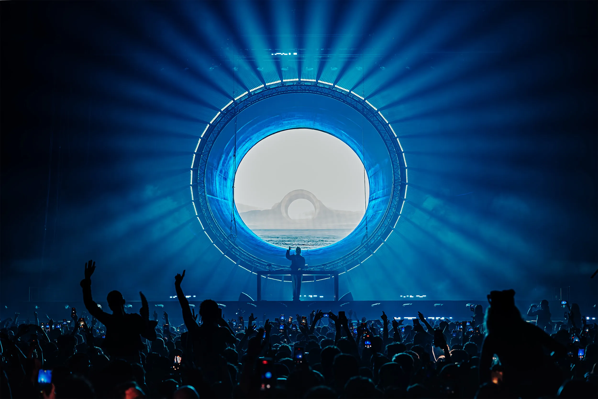 Sub Focus framed by a large circular portal of blue beams, a misty landscape on the screen inside